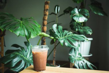 Ahşap bir masaya yerleştirilmiş plastik bardakta buzlu kakao. arkaplan dikilen ağaçlarla dekore edildi