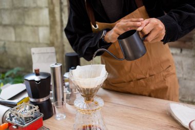 Adam kahve yapmak için bardağa sıcak kahve damlatıyor, ekipmanla, mutfak evinde demlenen aletle.