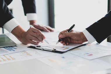 Toplantıda iki iş adamının buluşup belgeleri tartışması ve verileri göstermesi.