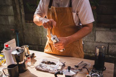 Adam öğütülmüş Arap fasulyelerinden taze bir bira hazırlıyor. Kırsal bir kafede elle paslanmaz çelik öğütücüye. Lezzetli ve aromatik bir kahve deneyimi.
