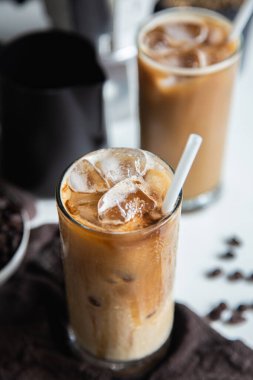 Dikey fotoğraf, cam bardakta buzlu kahve fincanı kavrulmuş kahve ve ahşap masada İtalyan moka kahve demliği.