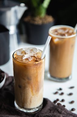 Dikey fotoğraf, cam bardakta buzlu kahve fincanı kavrulmuş kahve ve ahşap masada İtalyan moka kahve demliği.