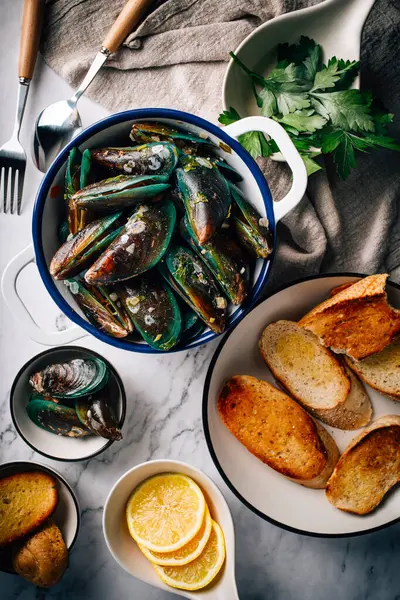 Doğranmış sarımsak, domates, limon ve otlarla servis edilen taze pişmiş midyeler denizden tabağınıza Fransız ekmeği ile süslenmiş lezzetli deniz ürünleri tabağı. Dikey fotoğraf üst görünümü