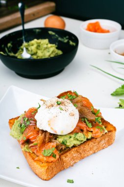 Haşlanmış yumurtalı kahvaltı tabağı, kızarmış somon guacamole tostu ev yapımı sağlıklı ve ekmekle servis ediliyor. Dikey fotoğraf