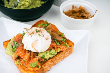 Haşlanmış yumurtalı kahvaltı tabağı, kızarmış somon guacamole tostu ev yapımı sağlıklı ve ekmekle servis ediliyor..