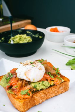 Haşlanmış yumurtalı kahvaltı tabağı, kızarmış somon guacamole tostu ev yapımı sağlıklı ve ekmekle servis ediliyor. Dikey fotoğraf