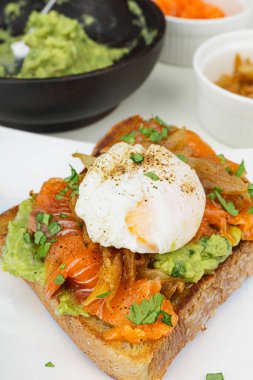 Haşlanmış yumurtalı kahvaltı tabağı, kızarmış somon guacamole tostu ev yapımı sağlıklı ve ekmekle servis ediliyor. Dikey fotoğraf