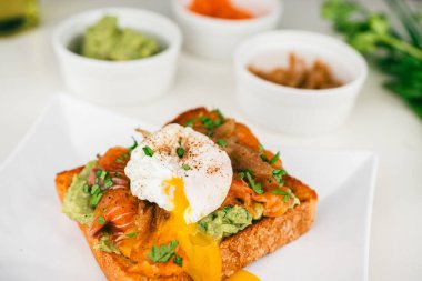  Haşlanmış yumurtalı taze kahvaltı tabağı, akıcı yumurta sarısı, füme somon guacamole tostu ev yapımı sağlıklı ve ekmekle servis edilmiş..