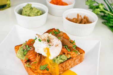  Haşlanmış yumurtalı taze kahvaltı tabağı, akıcı yumurta sarısı, füme somon guacamole tostu ev yapımı sağlıklı ve ekmekle servis edilmiş..