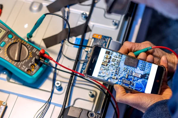 Electronics technician analyzes the components with his mobile phone and a tester.