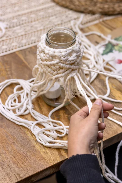 Macrame. The art of knot tying. Middle-aged woman weaving on a glass jar with this technique.