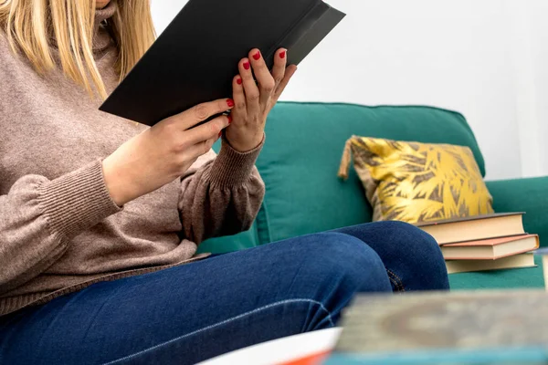 International Book Day. Young woman sitting on sofa reading a black book.
