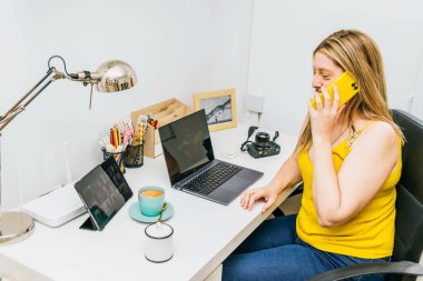 Ev ofisinde çalışan bir kadın telefon ve dizüstü bilgisayar kullanıyor. Evden çalışıyor. Telesekreter konsepti..