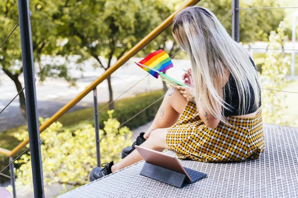 LGTBI üniversiteli kız. Modern dövmeli kız üniversitede gurur bayrağıyla not alıyor.