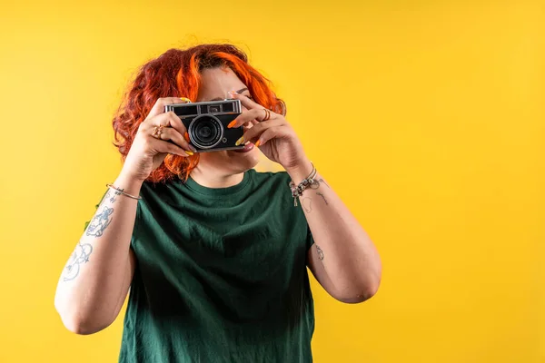 Modern tattooed non-binary redhead girl taking a photo of you with an old camera.
