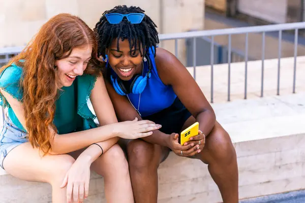 stock image Interracial and multicultural friendship. Two friends looking at their cell phones on the street