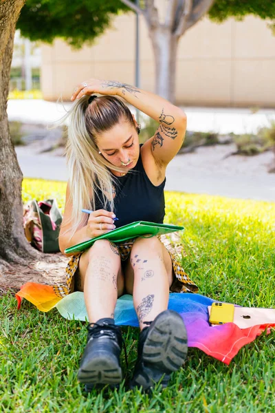 Back to School. Modern student with tattoos studies sitting in the university garden on a LGTBI flag