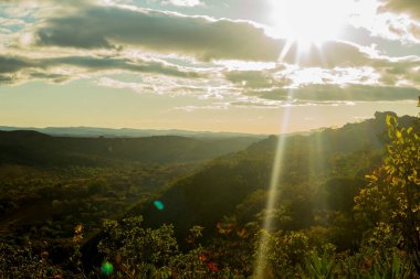 Güneş, bitki ve kayalarla kaplı bir dağ.