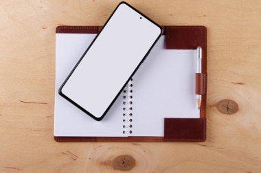 Dijitalleştirme kavramı. Kağıt defter akıllı telefona karşı. Boş beyaz ekranlı ve boş çizim defterli dijital telefon ahşap masanın üzerinde.
