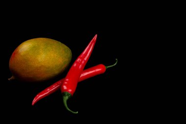 Whole mangoes and chili pepper on black background.