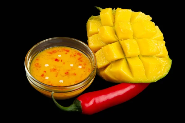 Cutted mango, chili pepper and mango chili sauce isolated on black background. Soft focus