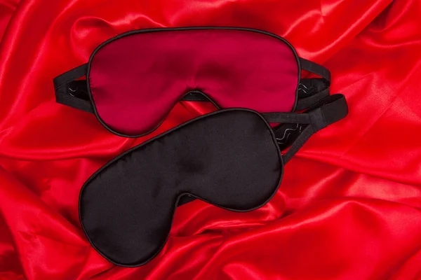 Two silk sleep mask lie on bright red silken background. Concept of eye protection from light for good sleep and melatonin production