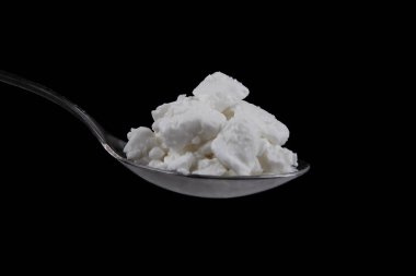 Cottage cheese in metal spoon isolated on black background. Side view of Curdled milk solids