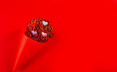 Mini krakerler ve kırmızı arka planda duran kırmızı kağıt külahta küçük renkli kalpler. Kraker pazarı konsepti. Kopyalama alanı olan pankart