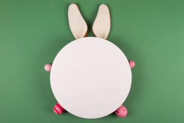 Paskalya yumurtaları, beyaz daireler ve tavşan kulakları yeşil arka planı süslüyor.