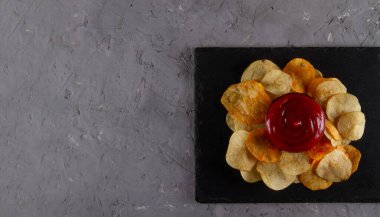 Gri alçı masa üzerinde servis panosunda kırmızı soslu patates cipsi yığını manzarası. Gurme Patates cipsi görüntüsü