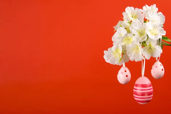 stock image Festive Easter scene captures the essence of spring with three pink Easter eggs hanging from a flowering branch set against orange background