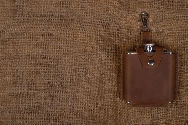 Hip flask in full grain leather case on sackcloth background. Banner with copy space for text place