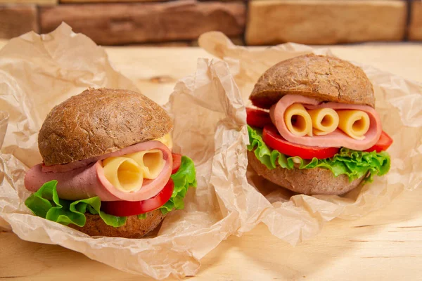 Апетитні Бутерброди Шинкою Сиром Свіжим Салатом Подаються Папері Випічки Дерев — стокове фото
