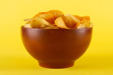 Sarı arka planda izole edilmiş killi kasede patates cipsi. yan görünüm