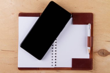 Dijitalleştirme kavramı. Kağıt defter akıllı telefona karşı. Boş siyah ekranlı ve boş defterli dijital telefon ahşap masanın üzerinde.
