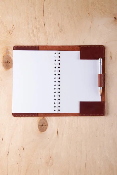 Blank writing-pad in leather cover with graphite pencil lie on wooden desk