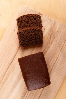 Siyah ekmek somunu ve dilimlenmiş muadili açık bej ahşap yüzeyde sunuluyor.