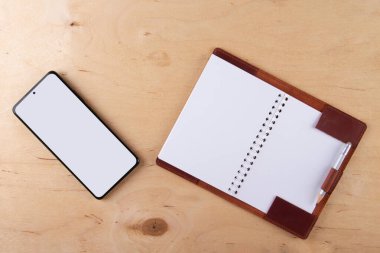 Dijitalleştirme kavramı. Kağıt defter akıllı telefona karşı. Boş beyaz ekranlı dijital telefon ve ahşap masaya uzanmış boş jotter.