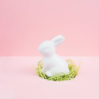 Yeşil çimenli bir yuvada oturan Paskalya tavşanı ya da tavşan. Bahar tatili tebrik kartı, pembe pastel renk, minimalizm. 