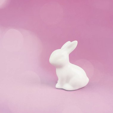 Easter bunny or rabbit sitting on a pink pastel colored background, spring holiday greeting card, bokeh light 