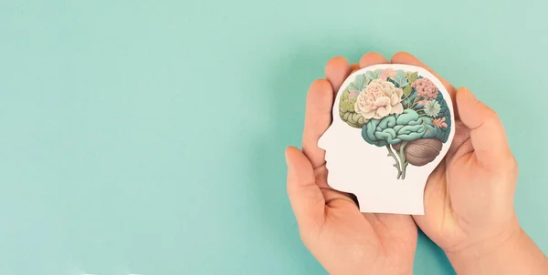 Hands holding paper head, human brain with flowers, self care and mental health concept, positive thinking, creative mind