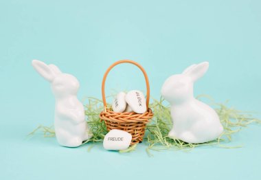 Wicker basket and easter bunny, words like love, luck and joy are standing in german language on the pebbles, rabbit brings gift and wishes