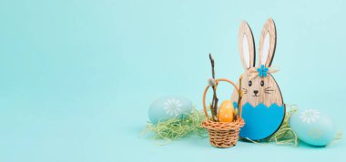 Easter bunny or rabbit sitting next to a wicker basket filled with colorful eggs, spring holiday 