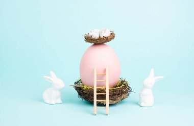 Easter bunny or rabbit sitting next to a huge pink colored egg in a birds nest, gift ribbon and ladder, spring holiday 