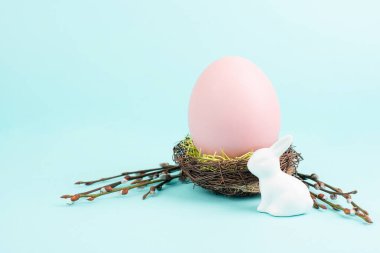 Easter bunny or rabbit sitting next to a wicker nest filled with colorful egg, spring holiday 