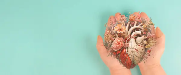 Hands holding human heart with flowers, love and emotion concept, good hearted person, help and charity