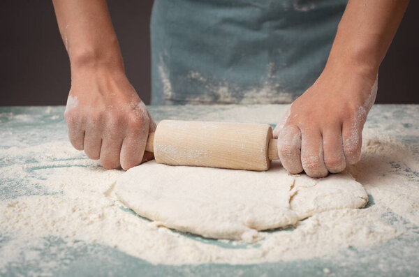 Baker rolls out dough for pizza, flatbread or pastry with rolling pin, prepare ingredients for food, baking for holidays