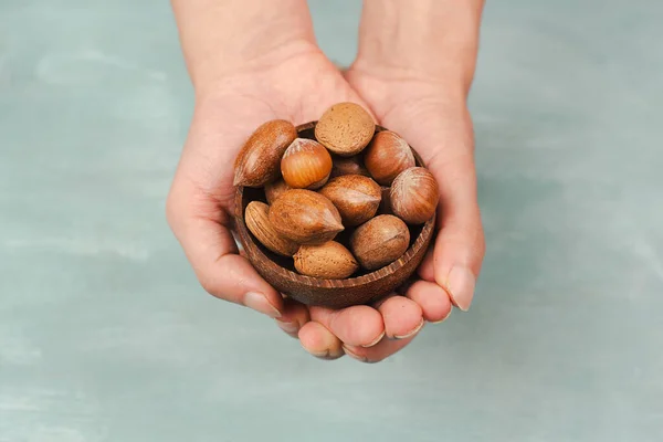 Holding a bowl of nuts, mix variety of almonds, hazelnuts and pecan nuts, healthy food and lifestyle