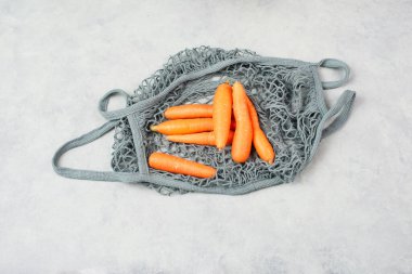 Yeniden kullanılabilir bir alışveriş poşetinde taze havuç, marketten alınmış sebze, sağlıklı yiyecek ve sıfır atık.