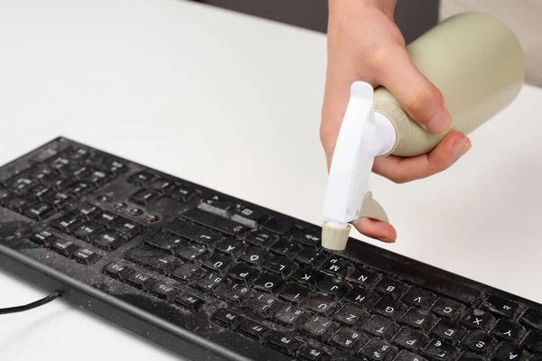 Cleaning computer keyboard in office, spraying water with a spray bottle dusty and dirty electronic, housework